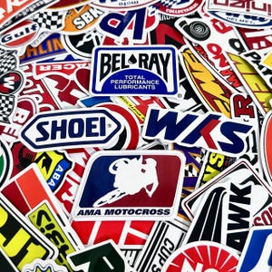 May include: A collection of colorful stickers featuring various logos and designs. Notable stickers include "BEL-RAY Total Performance Lubricants," "SHOEI," and "AMA MOTOCROSS." The stickers are a mix of shapes and sizes, with a focus on racing and automotive themes.