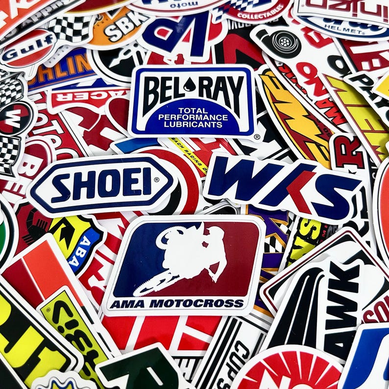 May include: A collection of colorful stickers featuring various logos and designs. Notable stickers include "BEL-RAY Total Performance Lubricants," "SHOEI," and "AMA MOTOCROSS." The stickers are a mix of shapes and sizes, with a focus on racing and automotive themes.