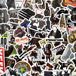 Può includere: Una collezione di adesivi assortiti con temi militari e tattici. Gli adesivi raffigurano vari personaggi, armi e testo, tra cui "SCAVS", "PRAPOR" e "GARK". La tavolozza dei colori include sfumature di nero, grigio, marrone e rosso.
