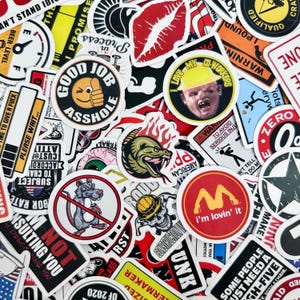May include: A selection of vibrant stickers with diverse designs and text. Features a sticker with a thumbs-up emoji and the words "GOOD JOB ASSHOLE". Other stickers include a snake, a rat, and the phrase "I'm lovin' it".