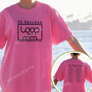 May include: A pink t-shirt featuring the text "Ed Sheeran Loop Tour North America 2026" in black. The design includes a cassette tape graphic. The back of the shirt also has tour dates.