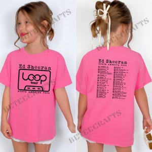 May include: A bright pink t-shirt featuring the text "Ed Sheeran Loop Tour North America 2026" in black. The back of the shirt lists tour dates. The shirt is worn by a young person.