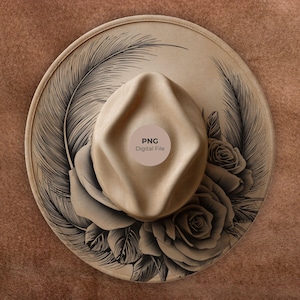 Op de afbeelding: Een beige fedora hoed met een brede rand, versierd met een zwart veren- en rozenontwerp. De hoed heeft een ronde sticker met de tekst "PNG Digital File". De hoed staat tegen een bruine achtergrond.
