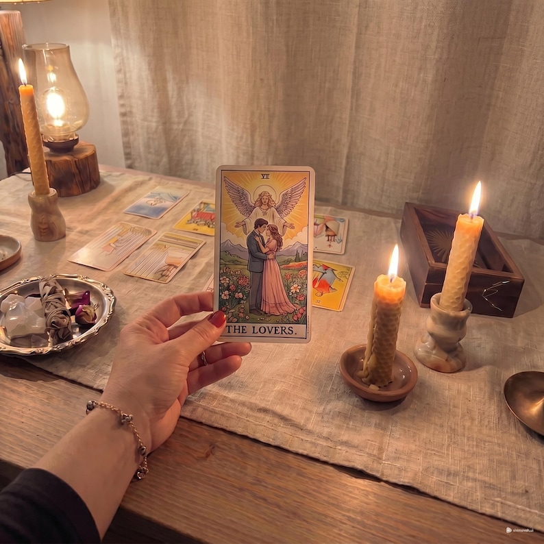 May include: A tarot card depicting "THE LOVERS" held in a hand, with other cards and lit candles on a wooden table. A decorative plate and a vintage lamp are also visible, creating a mystical atmosphere.