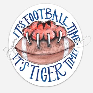 May include: A watercolor illustration on a white background. A brown football is beneath a tiger paw with orange and black stripes and long white claws. The text "IT'S FOOTBALL TIME! IT'S TIGER TIME!" is in blue.