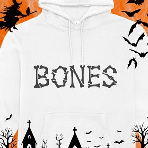May include: White hoodie with a black graphic of the word "BONES" in a skeletal font. The hoodie has a black drawstring and a black bat graphic on the right sleeve. The background is a blurry orange and black Halloween-themed design.