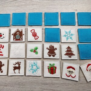 May include: A set of 18 felt Christmas-themed matching game tiles. The tiles are blue and white with various embroidered images, including a gingerbread house, a candy cane, a snowman, a snowflake, a star, a reindeer, a Christmas tree, a present, a Santa Claus, and a holly sprig.