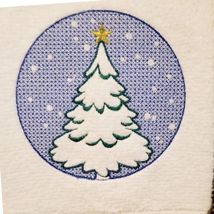 Könnte beinhalten: Weißes Handtuch mit gesticktem Weihnachtsbaum-Design. Der Baum ist weiß mit grünen Akzenten, gekrönt von einem goldenen Stern, vor einem blauen Hintergrund mit weißen Schneeflocken-Details. Das Handtuch hat einen strukturierten Rand.