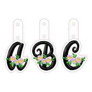 May include: Three black fabric letters with floral embellishments, A, B, and C, with white fabric loops at the top.