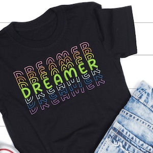 May include: Black t-shirt with a rainbow graphic of the word "Dreamer" repeated multiple times.