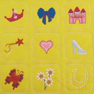 May include: Nine embroidered squares on a yellow background. Each square features a different princess-themed image: a crown, a bow, a castle, a wand, a heart, a glass slipper, a butterfly, flowers, and a necklace.