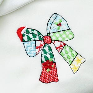 K&ouml;nnte beinhalten: Gestickte Weihnachtsschleife mit Patchwork-Design. Die Schleife hat rote, gr&uuml;ne, blaue und gelbe Abschnitte mit festlichen Mustern wie Weihnachtsb&auml;umen, Stechpalmen und Sternen. Die Schleife ist vor einem wei&szlig;en Hintergrund platziert.
