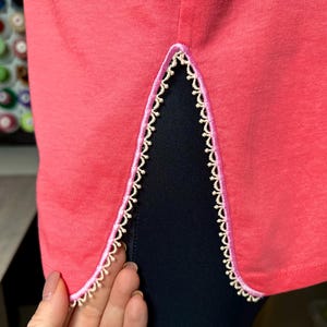 May include: A coral pink t-shirt with a side slit detail. The slit is trimmed with a white and pink lace.