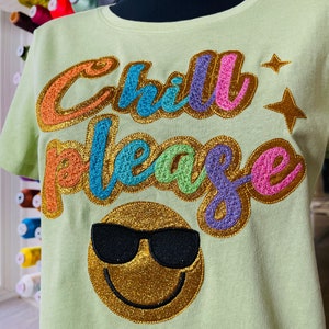 May include: A light green t-shirt with the text "Chill Please" in rainbow colors with gold glitter accents. A gold glitter smiley face with black sunglasses is below the text.