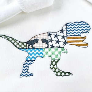 Puede incluir: Diseño de dinosaurio bordado sobre fondo blanco. El dinosaurio está compuesto por varios parches estampados, incluyendo estrellas, zigzags y patrones de cuadros en azul, verde y marrón. También se incluyen dos siluetas de dinosaurios más pequeñas.
