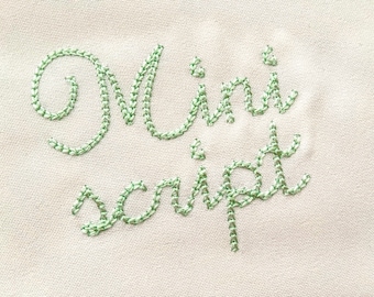 Op de afbeelding: Close-up van een crèmekleurige stof met de woorden "Mini script" geborduurd in lichtgroen garen. De borduursels hebben een delicate, handgemaakte uitstraling, waarbij elke letter zorgvuldig is gestikt.