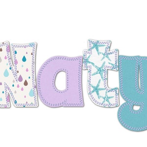 Peut inclure: Le nom "Naty" est écrit en lettres de tissu colorées. Le "N" est décoré d'un fond blanc et d'un motif de gouttes de pluie roses, bleues et brunes. Le "a" est de couleur violette unie. Le "t" est décoré d'un fond blanc et d'un motif d'étoiles de mer bleues. Le "y" est de couleur bleue unie.