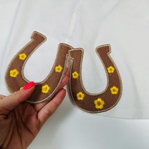 May include: Two brown felt horseshoe patches with yellow embroidered flowers.