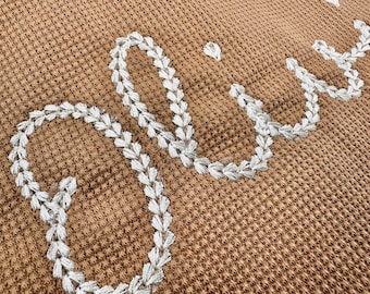 May include: A close-up of a brown waffle weave throw blanket with the word "Cozy" embroidered in white.