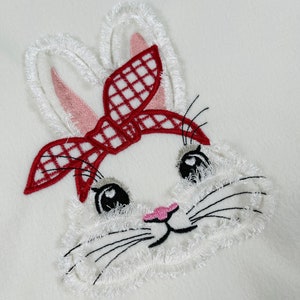 Puede incluir: Conejo blanco bordado con bandana a cuadros rojo y blanco, bigotes negros y nariz rosa.