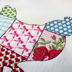 May include: A patchwork design of a chicken embroidered on a white fabric. The chicken is made up of different colored squares with patterns of hearts, bows, polka dots, and checkered designs.