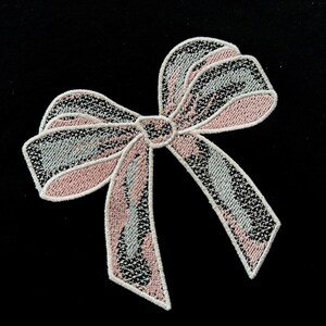 Puede incluir: Un delicado lazo de encaje blanco y rosa con un diseño en capas. El lazo es perfecto para agregar un toque de elegancia a cualquier proyecto.