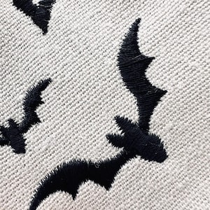 May include: A close-up of a gray fabric with black embroidered bats. The bats are in various positions, some flying and some upside down.