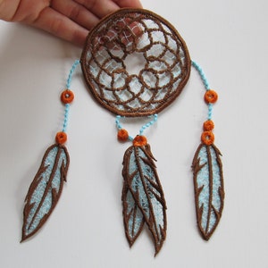 May include: A brown dreamcatcher with blue and white feathers and orange beads. The dreamcatcher is made of embroidery thread and is a popular Native American craft.