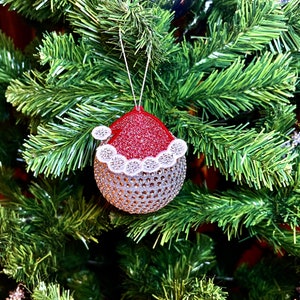 May include: A silver and red Christmas ornament shaped like a Santa hat with white trim and glitter. The ornament is hanging on a green artificial Christmas tree.
