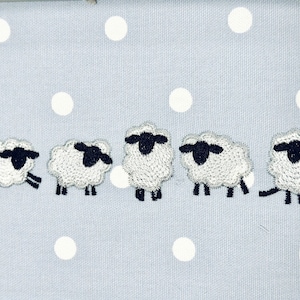 May include: Five white sheep with black faces and legs are embroidered on a light blue fabric with white polka dots.
