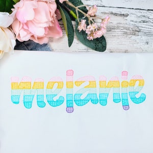 Puede incluir: Camiseta blanca con el nombre "Melanie" bordado en colores arcoíris.