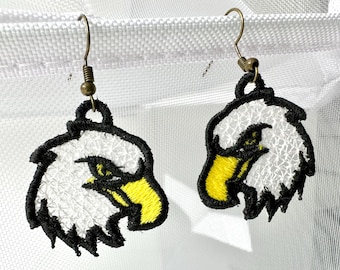 Puede incluir: Pendientes bordados con cabeza de águila. Los pendientes presentan una cabeza de águila blanca con contorno negro y pico amarillo. Cuelgan de ganchos para las orejas de color bronce.