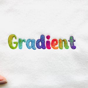 以下が含まれることがあります： 白い布地に虹色の糸で「Gradient」という単語が刺繍されています