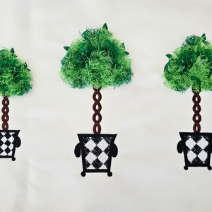 Puede incluir: Tres árboles topiarios en macetas de cuadros blancos y negros. Los árboles son verdes y tienen tallos marrones. Las macetas tienen un patrón de cuadros blancos y negros.