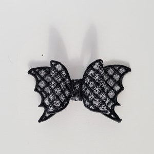 May include: A black bat-shaped hair bow with a white spiderweb pattern.