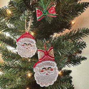 May include: Three handmade Christmas ornaments: a red and green bow, and two white lace Santa faces with red hats.