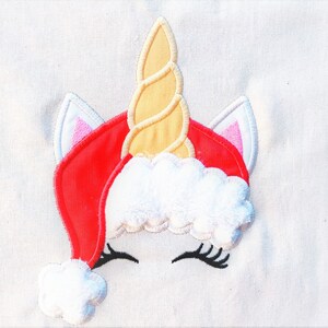 May include: Embroidered design of a unicorn wearing a red Santa hat with white fur trim and a yellow spiral horn.