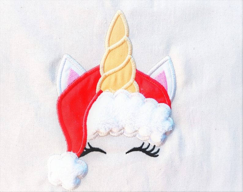 May include: Embroidered design of a unicorn wearing a red Santa hat with white fur trim and a yellow spiral horn.