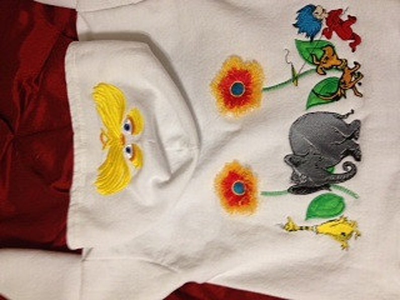 May include: White hooded sweatshirt with an embroidered design featuring the character of the Lorax, flowers, and characters from the book "The Lorax" by Dr. Seuss.