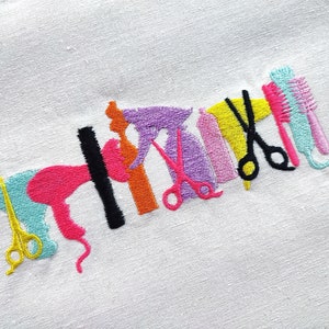 Puede incluir: Diseño bordado de varias herramientas de peluquería, incluyendo tijeras, un secador de pelo, un peine y una plancha de pelo. Las herramientas son de varios colores, incluyendo rosa, azul, amarillo, naranja y morado.