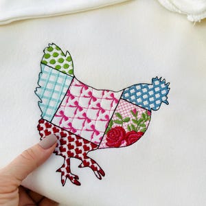 May include: A white fabric with a patchwork design of a chicken. The chicken is made up of squares of different colors and patterns, including red, pink, green, blue, and white.