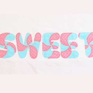 May include: The word "SWEET" is spelled out in large, colorful letters. Each letter is made of pink and blue fabric with a swirl pattern and white polka dots.