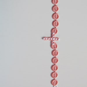 May include: A pink beaded rosary with a white cross charm.