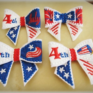 May include: Four red, white, and blue fabric bows with embroidered designs. The bows feature the text "4th" and "July" and images of fireworks and an American flag.