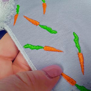 May include: A light purple fabric with embroidered green and orange carrots.