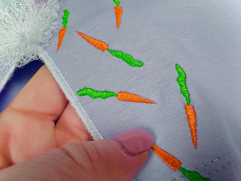May include: A light purple fabric with embroidered green and orange carrots.
