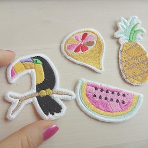 Pode incluir: Cinco patches bordados para passar a ferro que representam um tucano num ramo, um ananás, uma fatia de melancia e duas frutas cítricas. Os patches são coloridos e caprichosos.