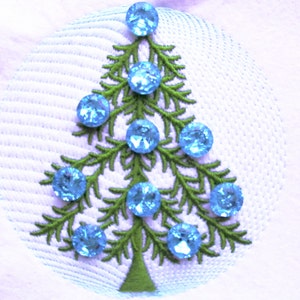 Op de afbeelding: Een groene geborduurde kerstboom met blauwe strasssteentjes op een witte achtergrond.