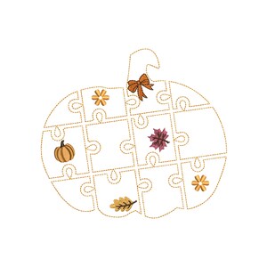 May include: A pumpkin-shaped puzzle with a gold outline, featuring a bow, a pumpkin, leaves, and flowers. The puzzle pieces are empty, and the design is embroidered on a white background. A fall-themed decorative item.