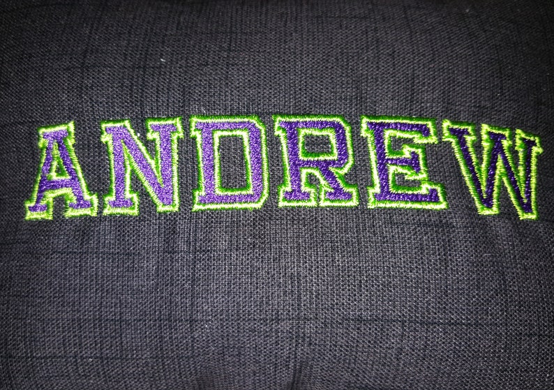 May include: A black fabric pillow with the name "ANDREW" embroidered in green and purple thread.